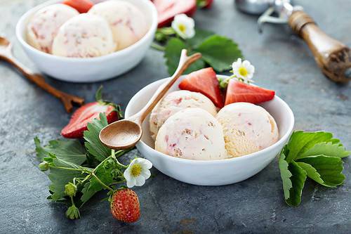 Horizontal side view of strawberry ice cream scoops in a white bowl.