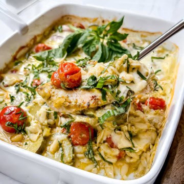Corner view of baked Caprese Pesto Chicken on a spatula for serving with cherry tomatoes and fresh basil.