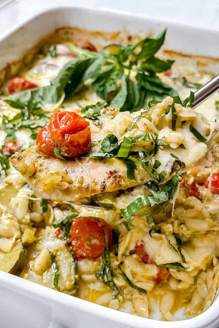 Corner view of baked Caprese Pesto Chicken on a spatula for serving with cherry tomatoes and fresh basil.