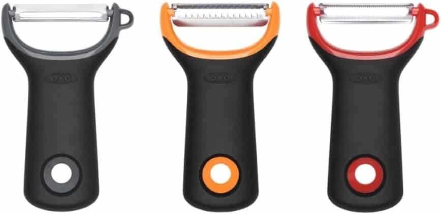 Three OXO vegetable peelers with black handles and different colored accents—gray, orange, and red—are shown side by side, each with a distinct blade style, perfect for preparing ingredients for your favorite salad recipes.
