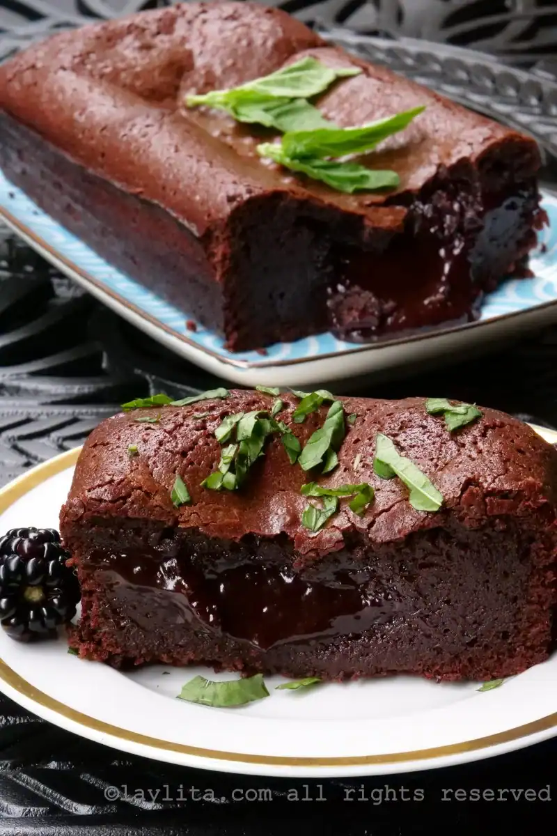 Two chocolate lava cakes with molten centers, a classic among French desserts, are garnished with fresh basil and served on plates-one with a slice cut out and a blackberry beside it.