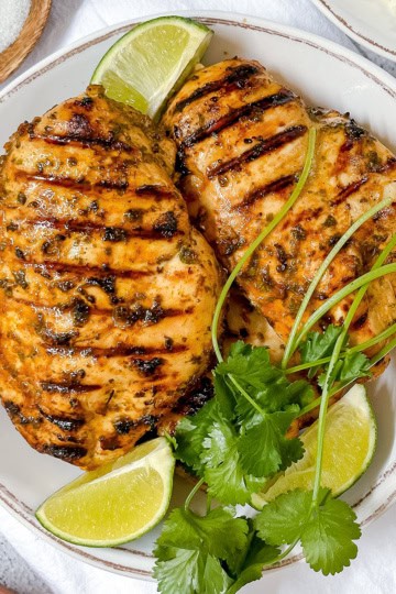Cilantro lime chicken breasts grilled to perfection, garnished with fresh cilantro and lime wedges, served on a white plate.