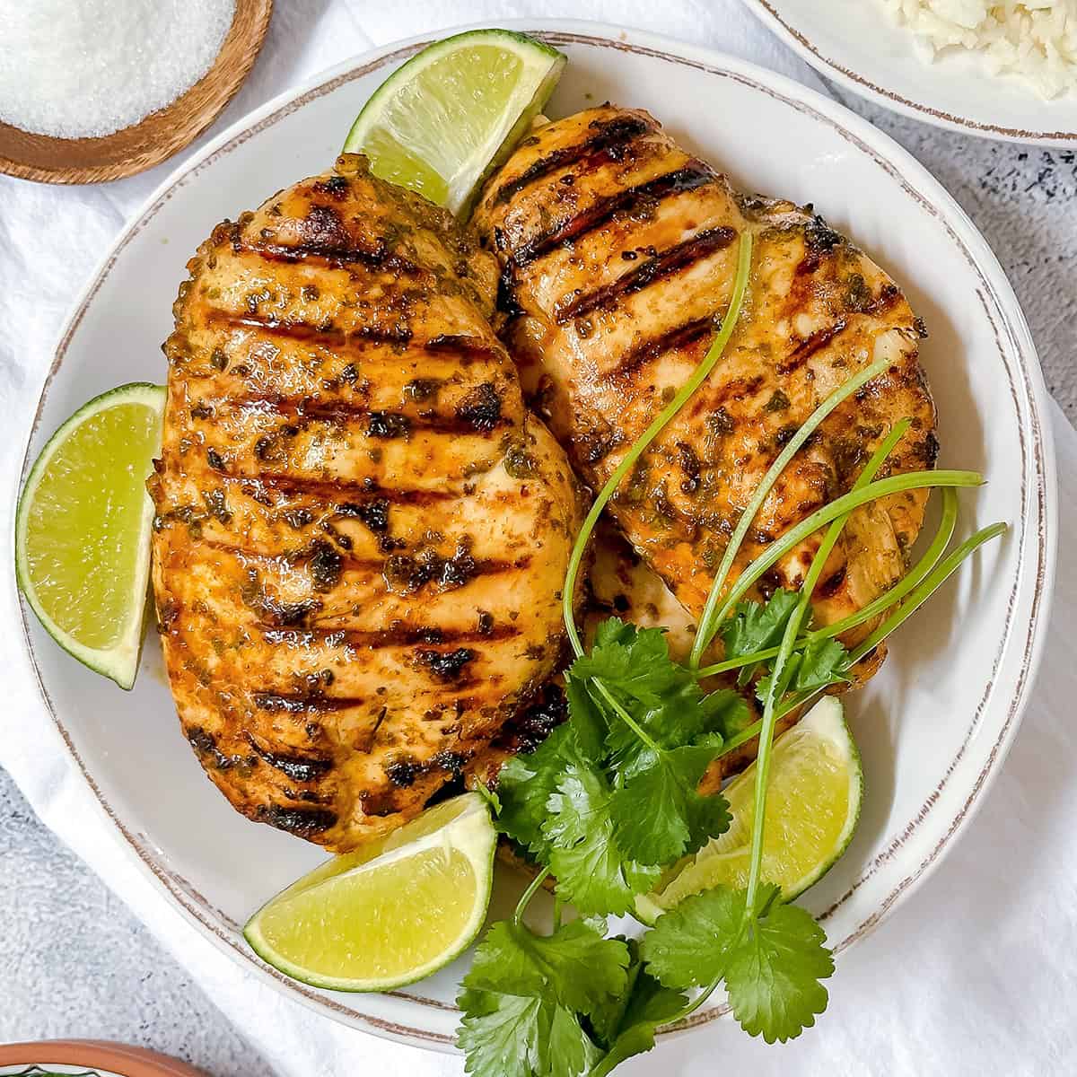 Cilantro lime chicken breasts grilled to perfection, garnished with fresh cilantro and lime wedges, served on a white plate.
