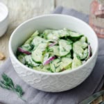Bowl of creamy cucumber salad with red onions and fresh dill.