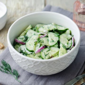 Bowl of creamy cucumber salad with red onions and fresh dill.