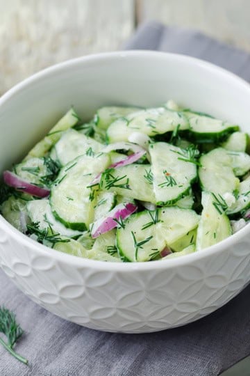 Bowl of creamy cucumber salad with red onions and fresh dill.