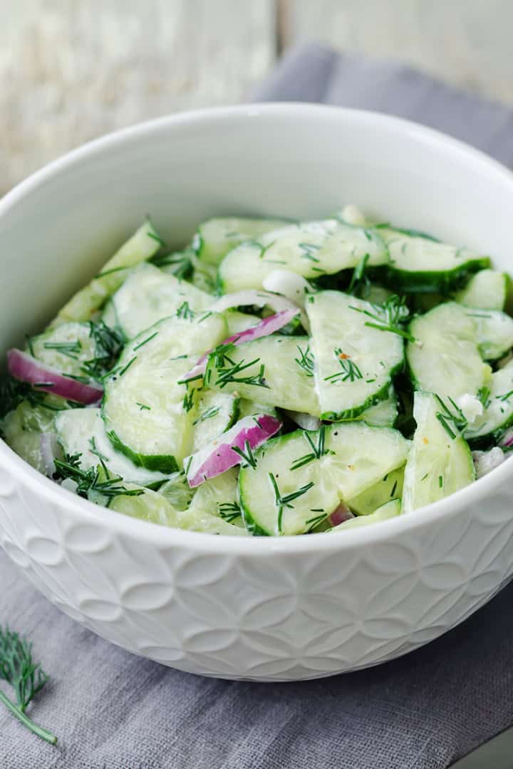Bowl of creamy cucumber salad with red onions and fresh dill.