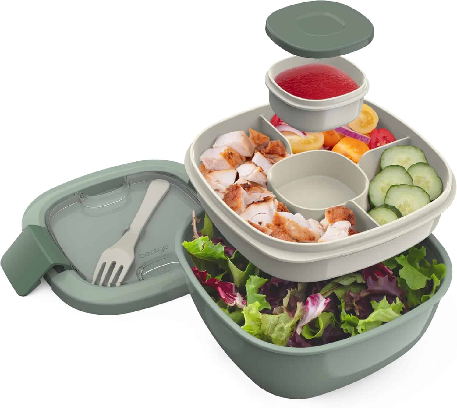 A green bento lunch box with compartments holds salad inspired by popular salad recipes, sliced grilled chicken, tomato, cucumber, and a small cup of red dressing, plus a lid and spork.