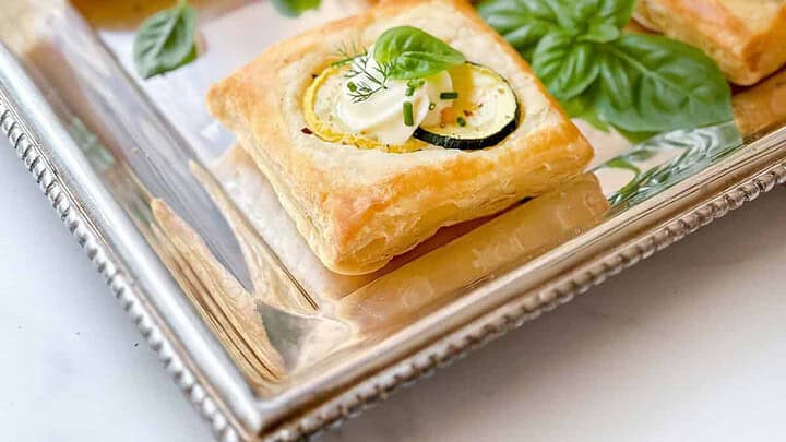 Side view of puff pastry savory tart on a silver square tray with fresh basil.