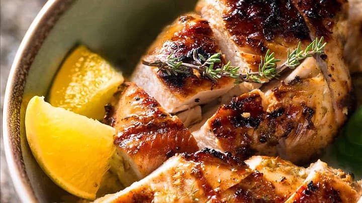 Closeup view of grilled chicken breast slices with fresh herbs.