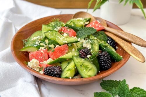 Horizontal view of watermelon salad in a wooden bowl with fresh mint leaves.