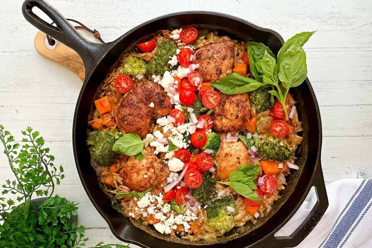 Top horizontal view of chicken orzo skillet in a black cast iron skillet with fresh basil.