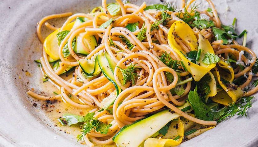 Top view of Mediterranean whole grain pasta with zucchini, summer squash and herbs in a white bowl.