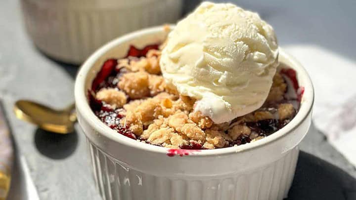 Side view of individual berry crisps with melting vanilla ice cream on a slate background.