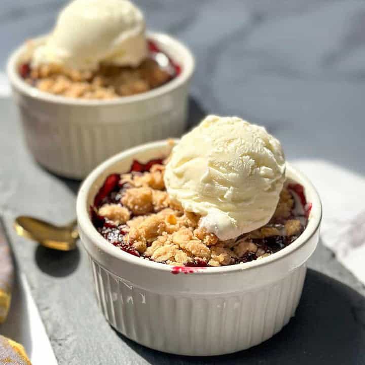 Side view of individual berry crisps with melting vanilla ice cream on a slate background.