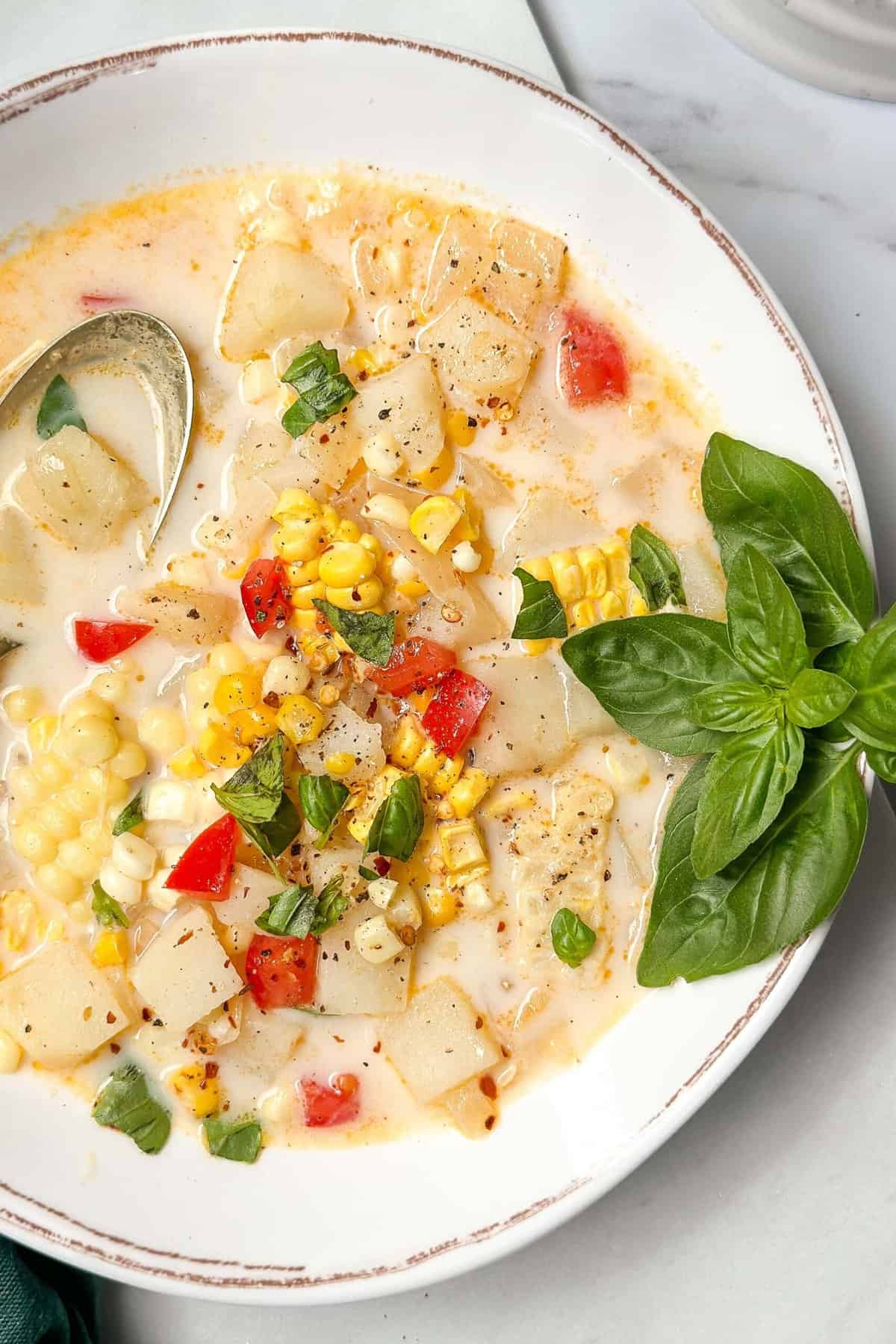 Closeup top view of a bowl of corn chowder in a white bowl and garnished with fresh basil.