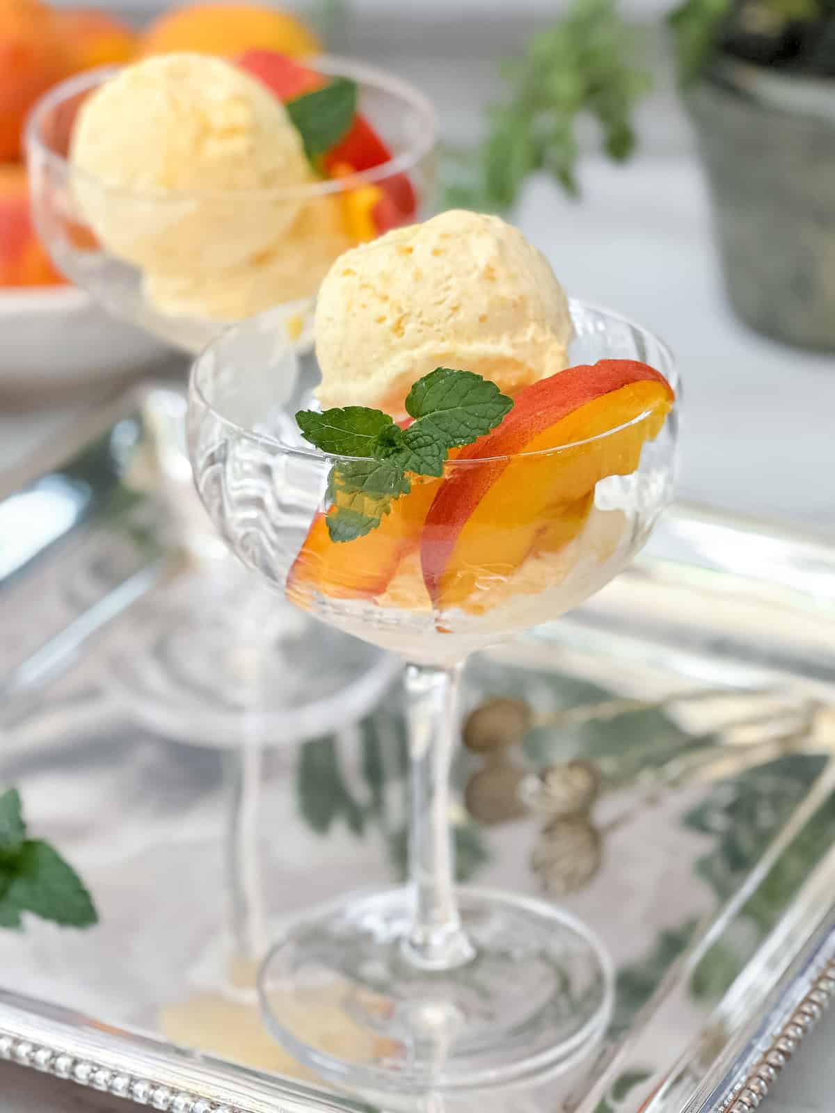 Two scoops of peach ice cream with fresh peach slices and mint on a silver tray.