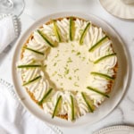 A ricotta cheesecake inspired key lime pie topped with whipped cream, lime wedges, and lime zest sits on a white plate on a marble surface.