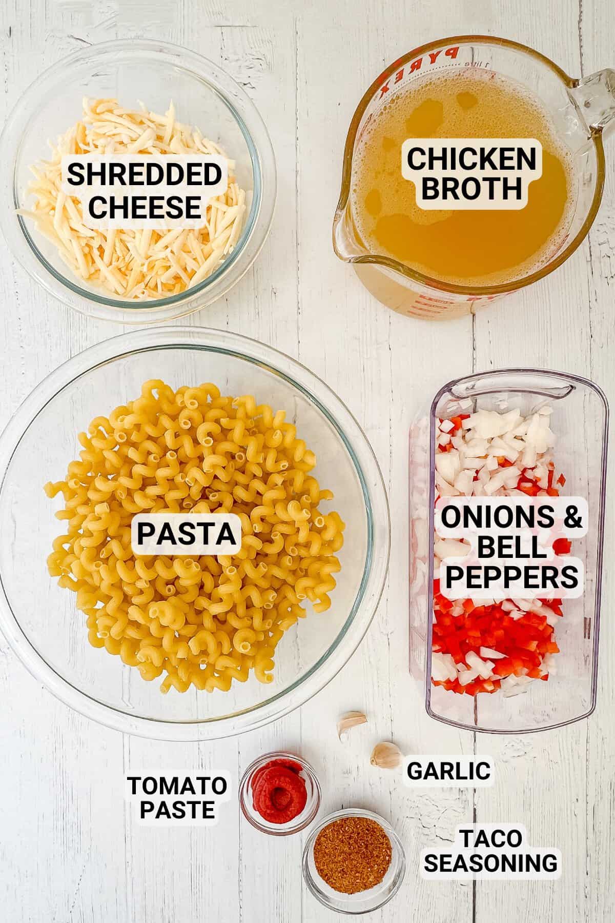 Ingredients for taco pasta: shredded cheese, chicken broth, uncooked pasta, chopped onions and bell peppers, tomato paste, garlic cloves, and taco seasoning, all labeled on a white background.
