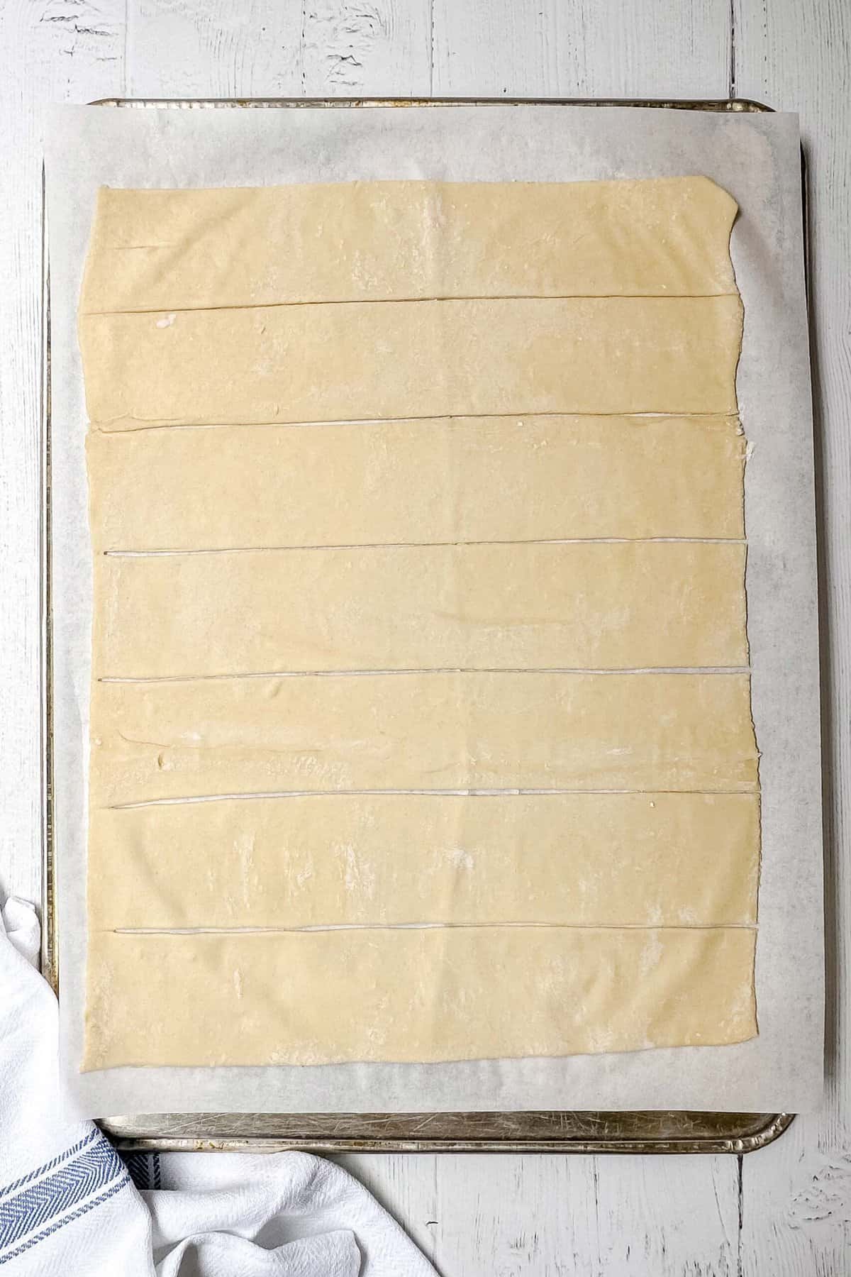 Top view of unbaked puff pastry rolled and cut into strips on parchment paper.