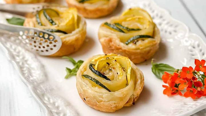 Closeup side view of tartlets on a serving platter with silver tongs.