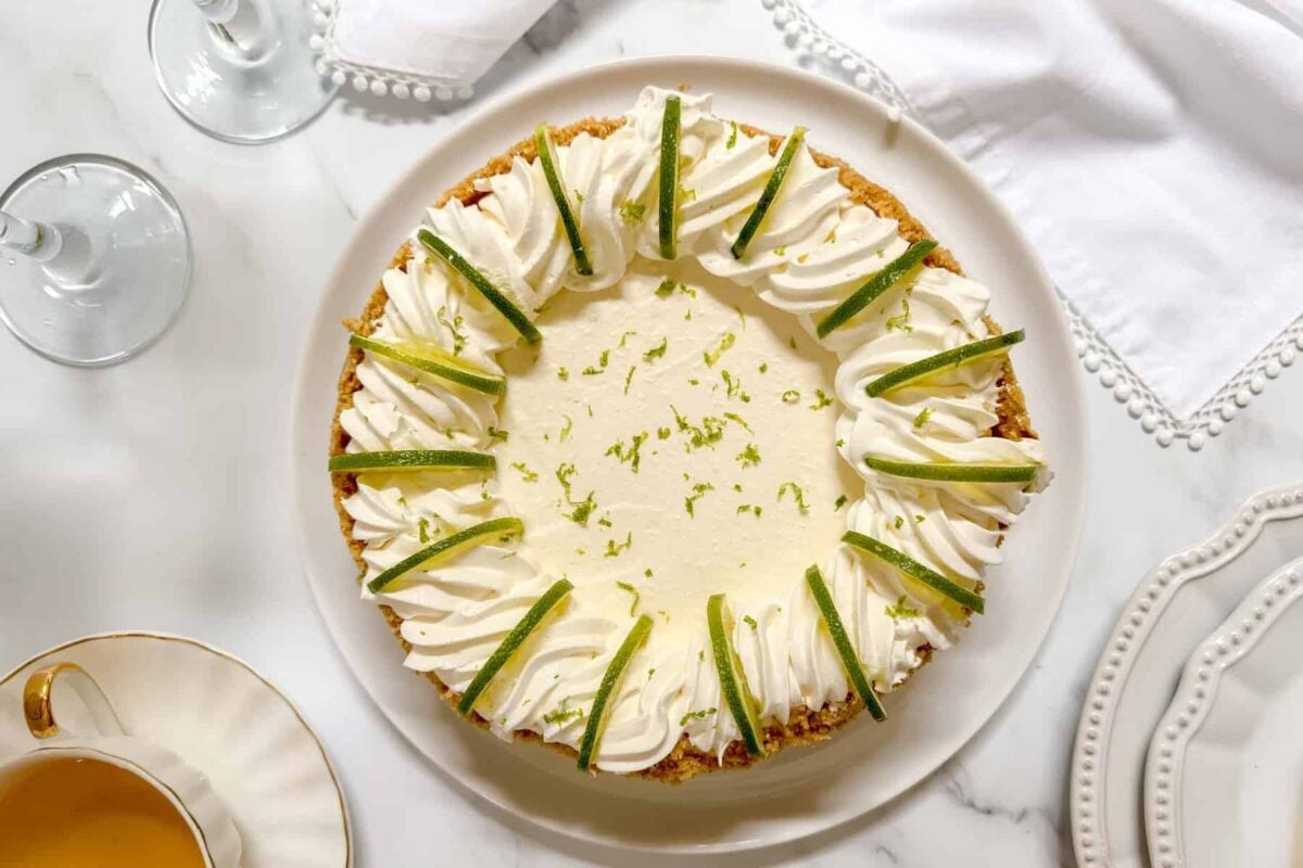 Top horizontal view of unsliced ricotta cheesecake with pipping, lime slices and lime zest.