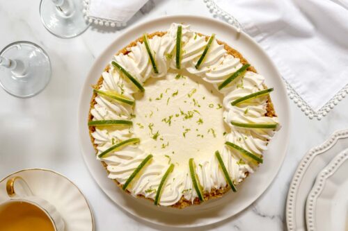 Top horizontal view of unsliced ricotta cheesecake with pipping, lime slices and lime zest.