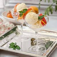 Horizontal side view of two homemade peach ice cream servings on a silver platter with fresh peaches and mint sprigs.