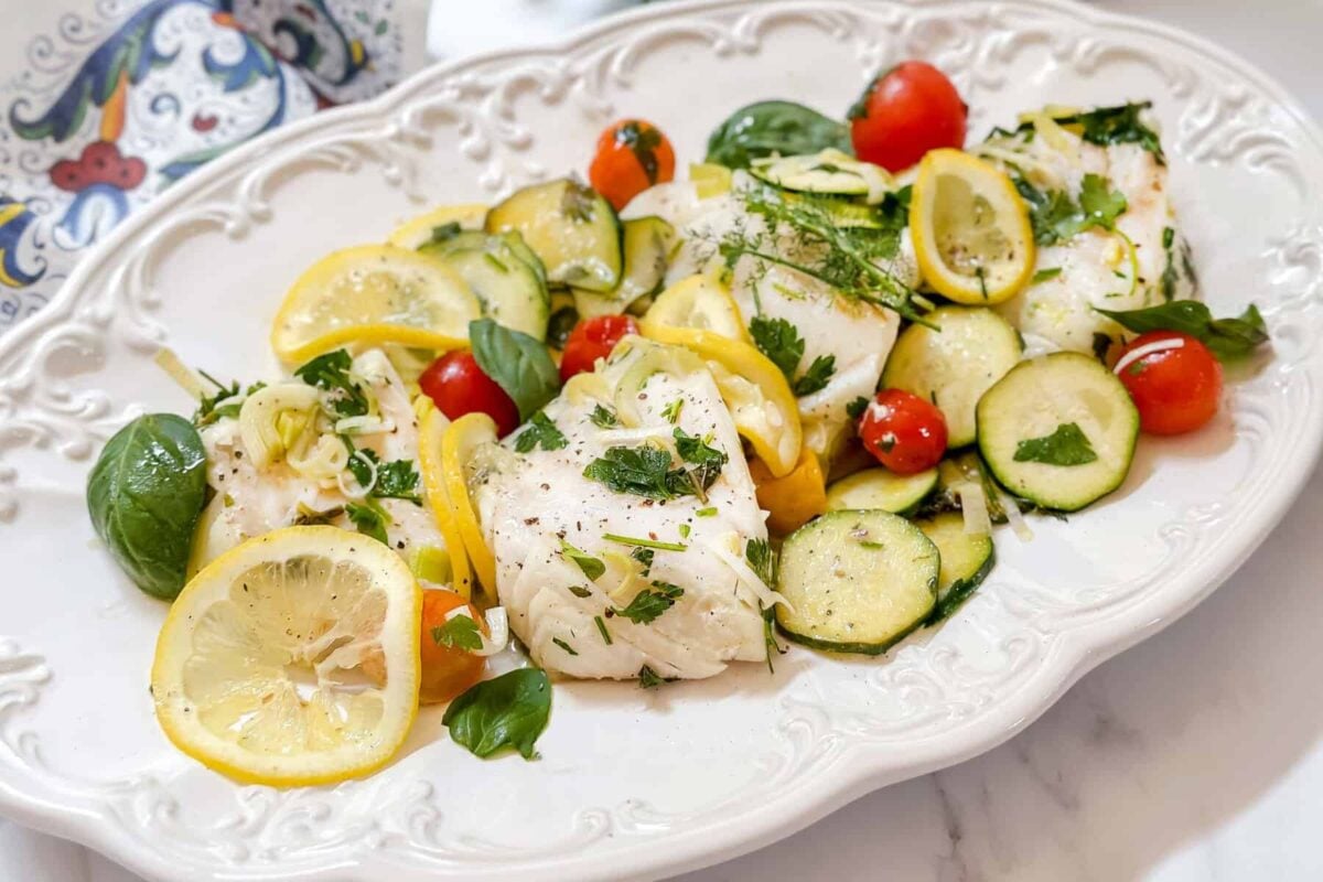 Horizontal closeup top view of steamed cod on a white serving platter.