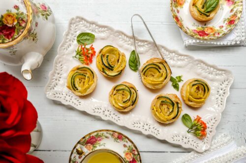 Top view of zucchini tartlets on a white scalloped serving platter for teatime.
