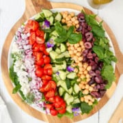 A large round platter with rows of chopped tomatoes, cucumbers, red onions, olives, chickpeas, feta cheese, and spinach-this stunning display celebrates the vibrant flavors of Mediterranean salads, garnished with fresh herbs and edible flowers.