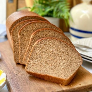 Sliced homemade whole wheat bread made in a single loaf and resting on a wooden sandwich board.