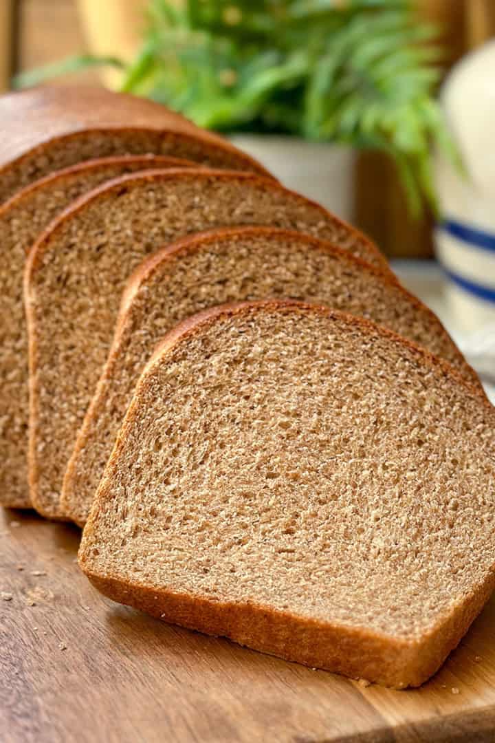 Sliced homemade whole wheat bread made in a single loaf and resting on a wooden sandwich board.