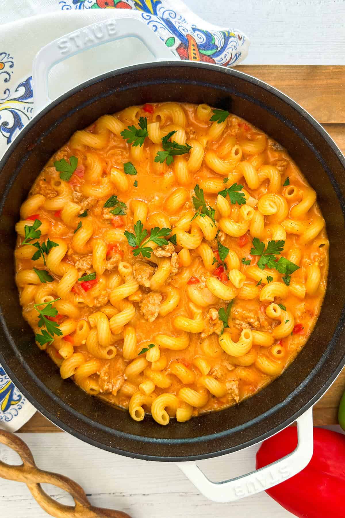 A pot of creamy taco pasta with ground meat and red peppers, garnished with parsley.
