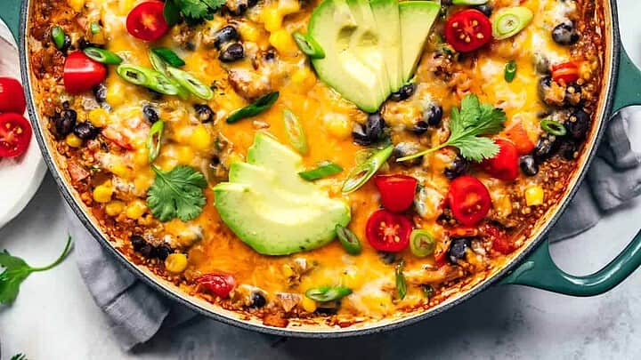 Top view of vegetarian taco skillet in a shallow braiser with fresh herbs, avocado and sliced green onions.
