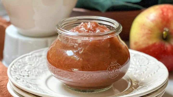 Side view of apple butter in a glass container with a bowl in the background.