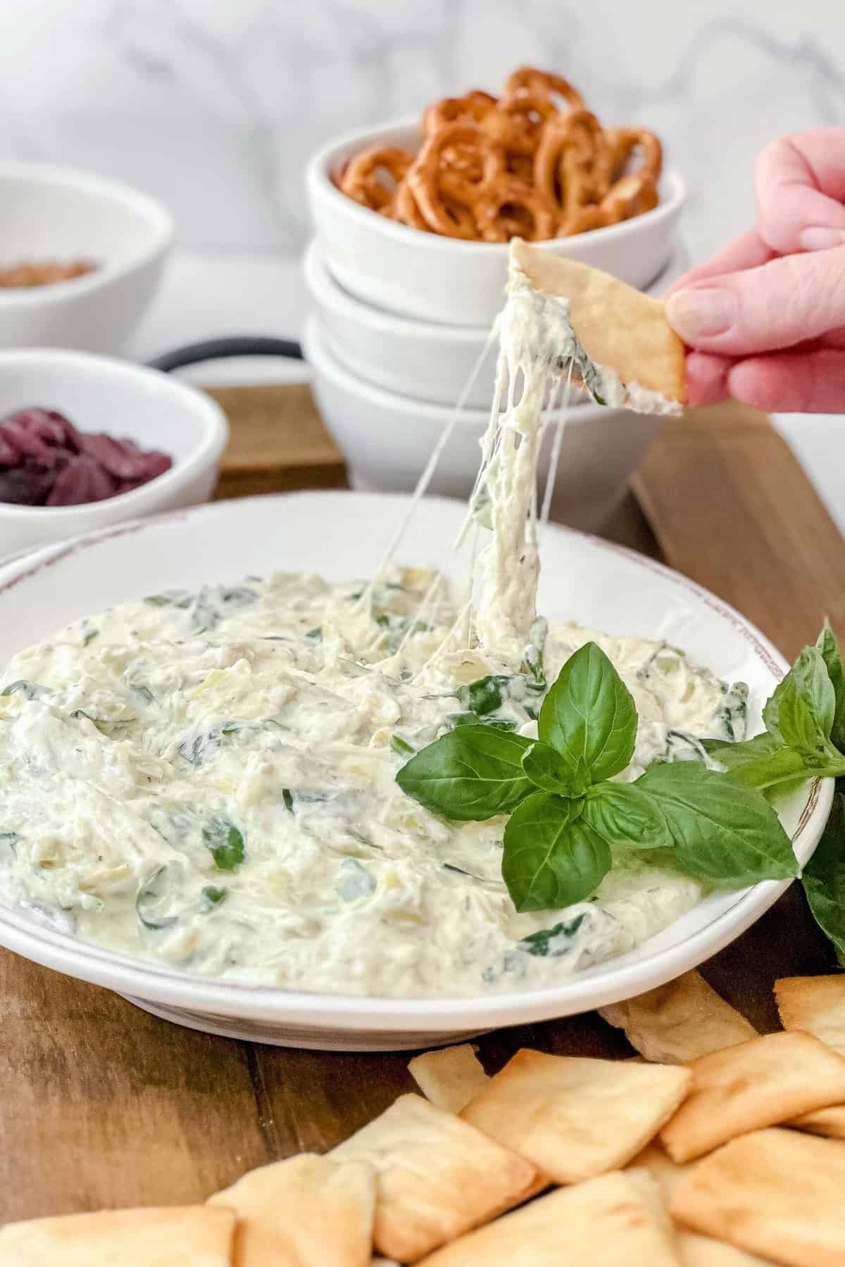 Side view of Spinach Artichoke Dip serving with a pita cracker on a wooden serving board.