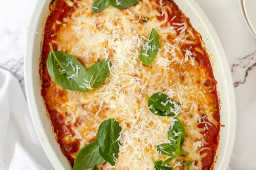 Top view of zucchini parmesan casserole with melting mozzarella cheese and fresh basil leaves.
