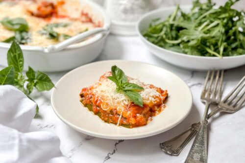 Horizontal side view of zucchini parmesan serving on a white plate with fresh basil.