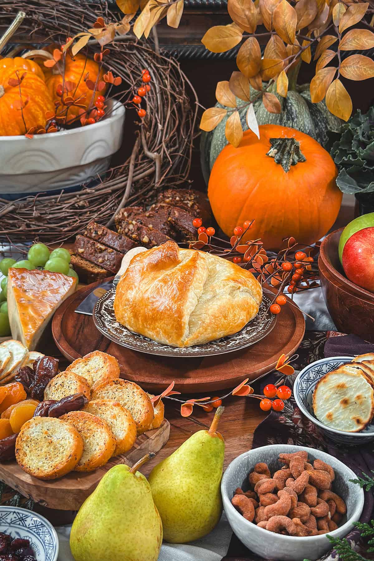 A fall charcuterie board or gazing board featuring baked brief in puff pastry, dried fruit, cheeses, crackers, nuts, and pumpkin bread.