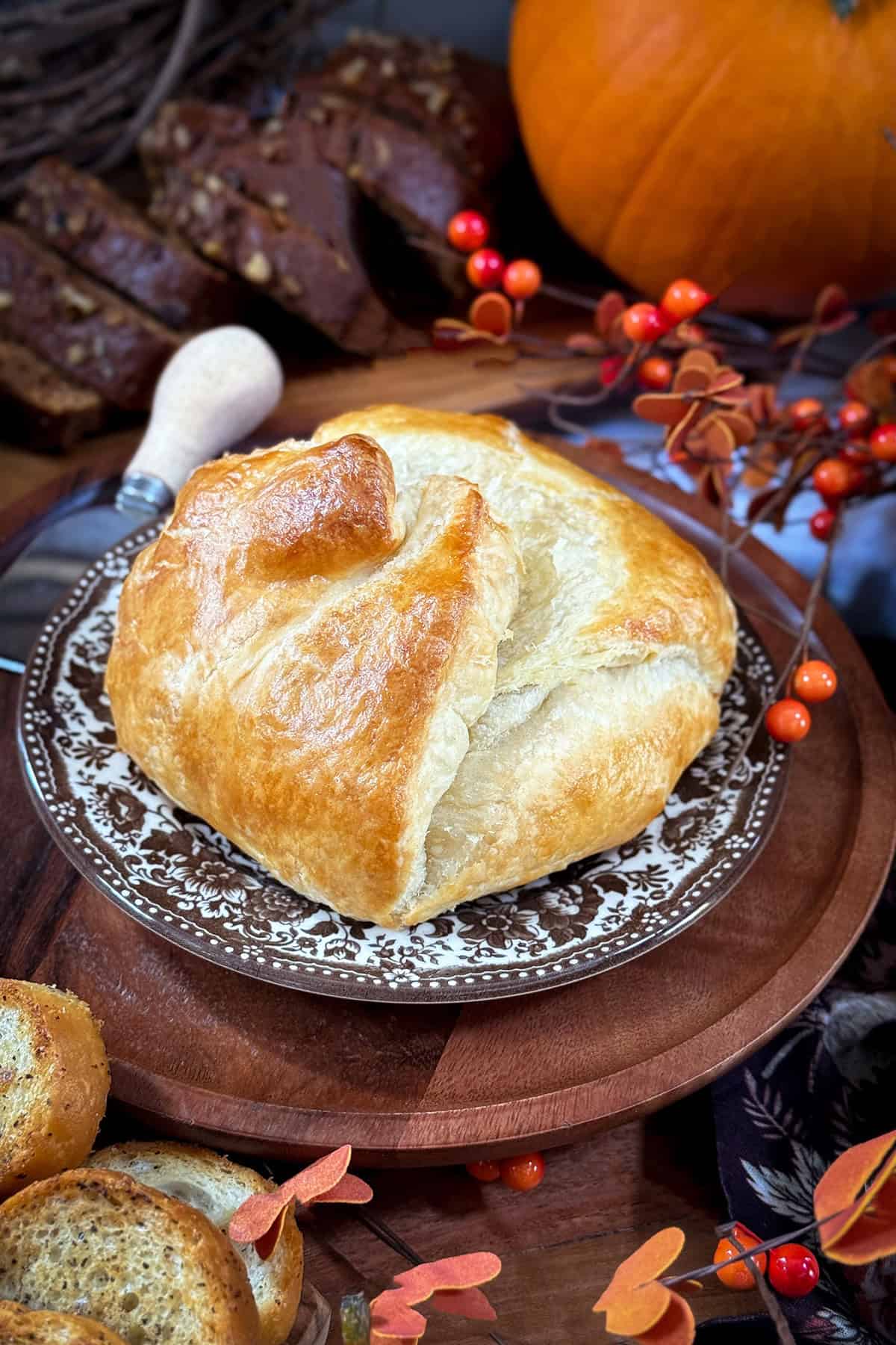Baked brie resting on a plate for serving in a fall charcuterie board or grazing board with a cheese knife nearby.