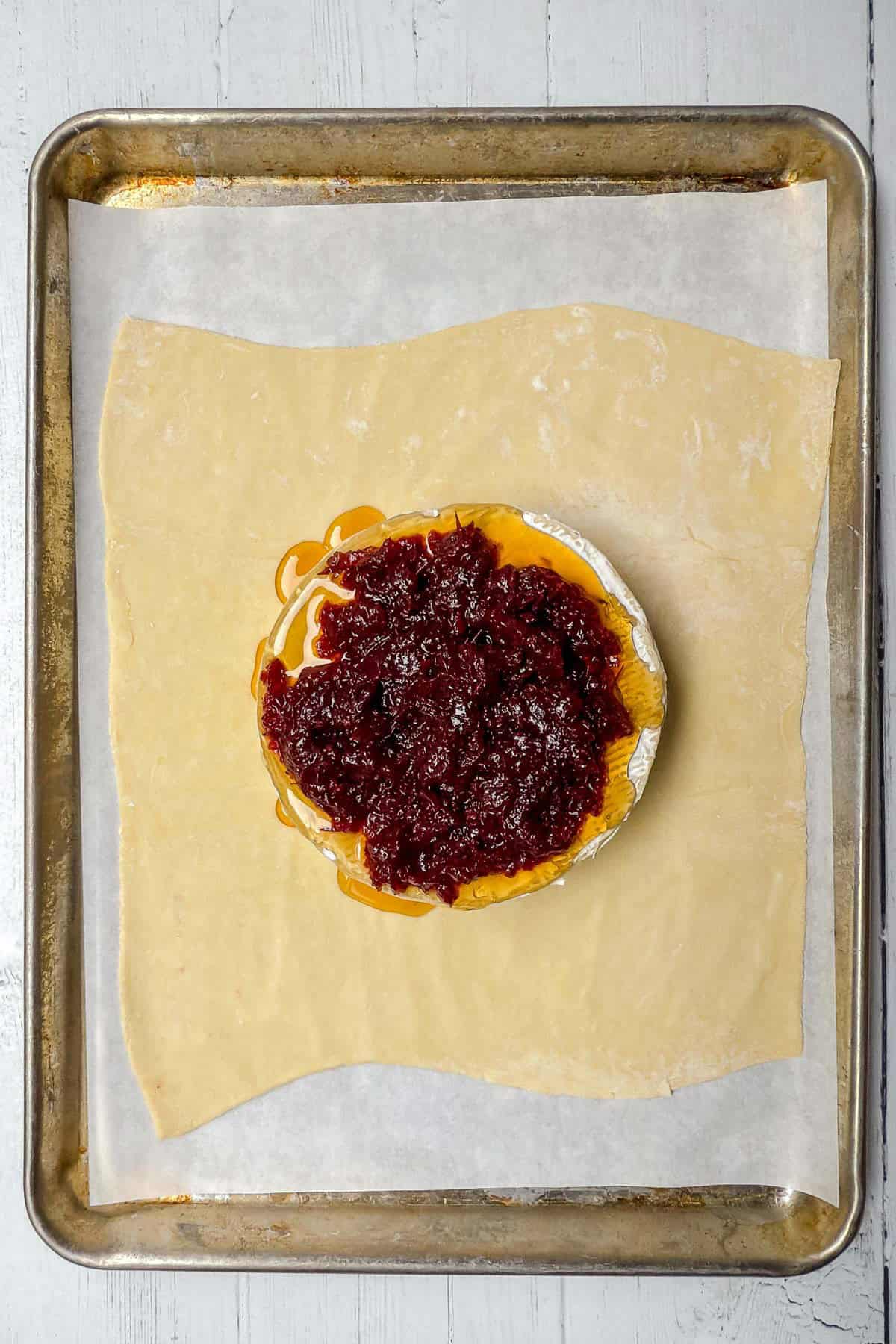 Cranberry sauce topos unbaked brie wheel with puff pastry underneath for folding and baking.