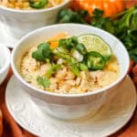 White Chicken Chili with butternut squash in a bowl with lime wedges, cilantro, and green onion toppings.