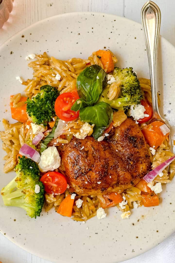 Dish of Mediterranean chicken thighs with vegetables, fresh herbs, and couscous cooked in a cast iron skillet.