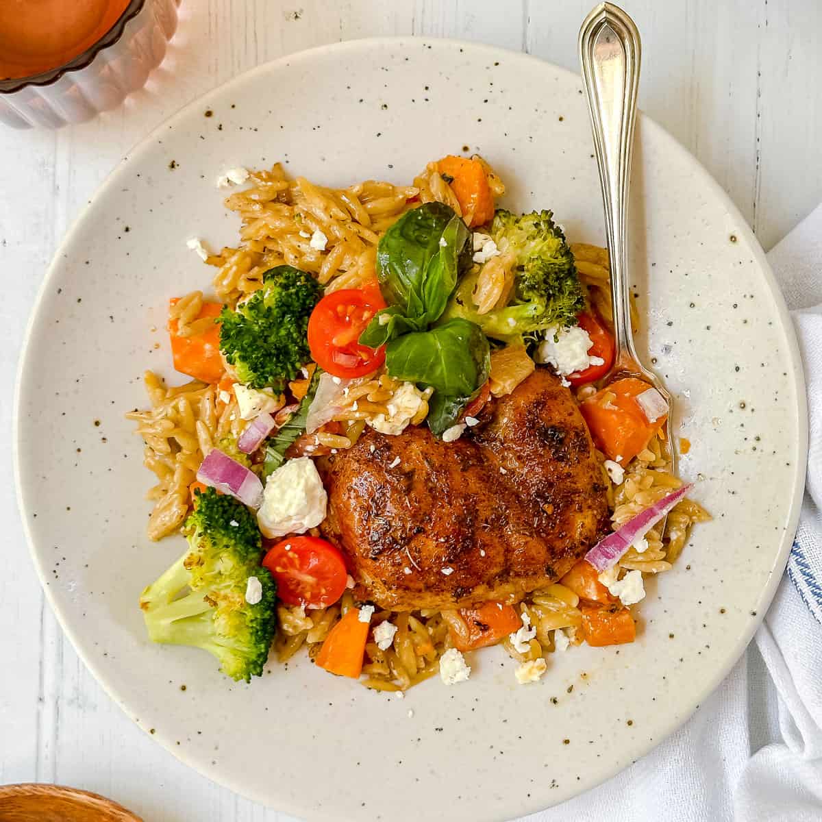 Dish of Mediterranean chicken thighs with vegetables, fresh herbs, and couscous cooked in a cast iron skillet.