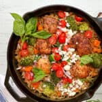 Mediterranean Chicken with fresh basil, feta, tomatoes, and couscous in a cast iron skillet.