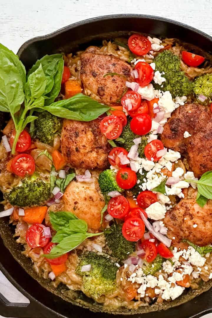 Mediterranean Chicken with fresh basil, feta, tomatoes, and couscous in a cast iron skillet.