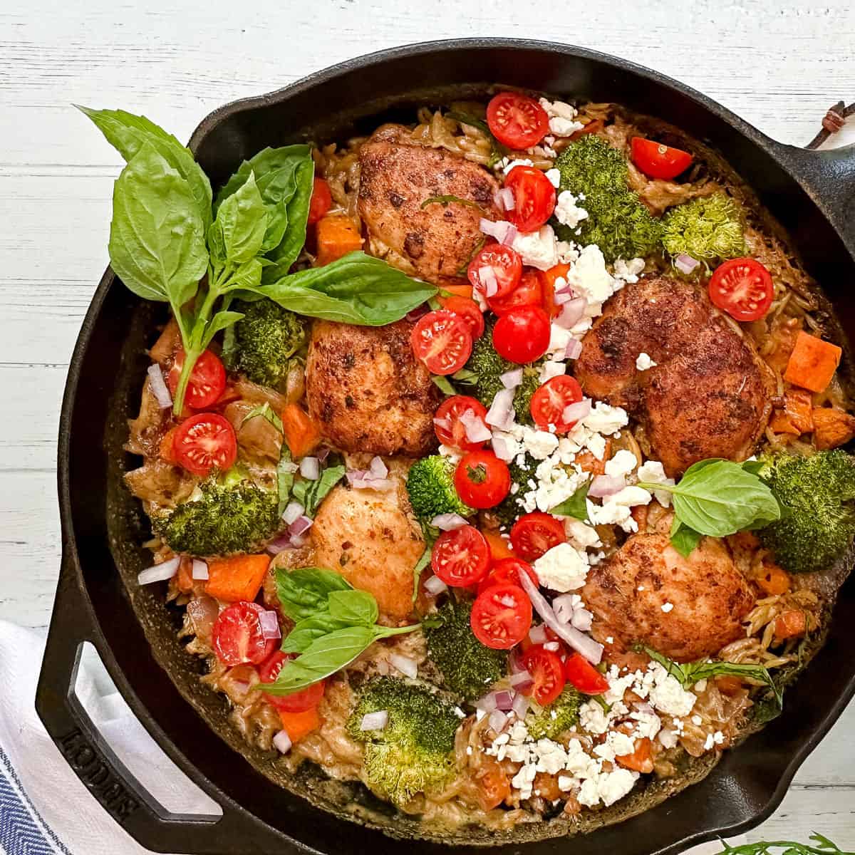Mediterranean Chicken with fresh basil, feta, tomatoes, and couscous in a cast iron skillet.