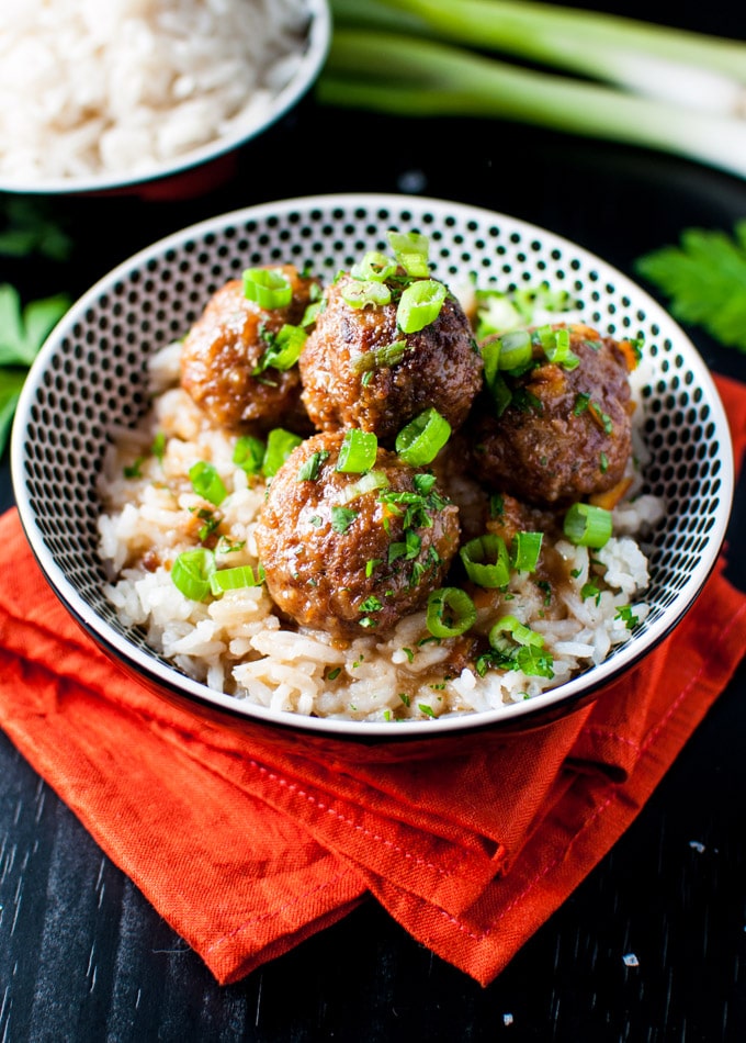 A bowl of white rice topped with four meatballs, garnished with chopped green onions and herbs, sits on an orange napkin-perfect comfort food for cozy Fall Slow Cooker Meals.