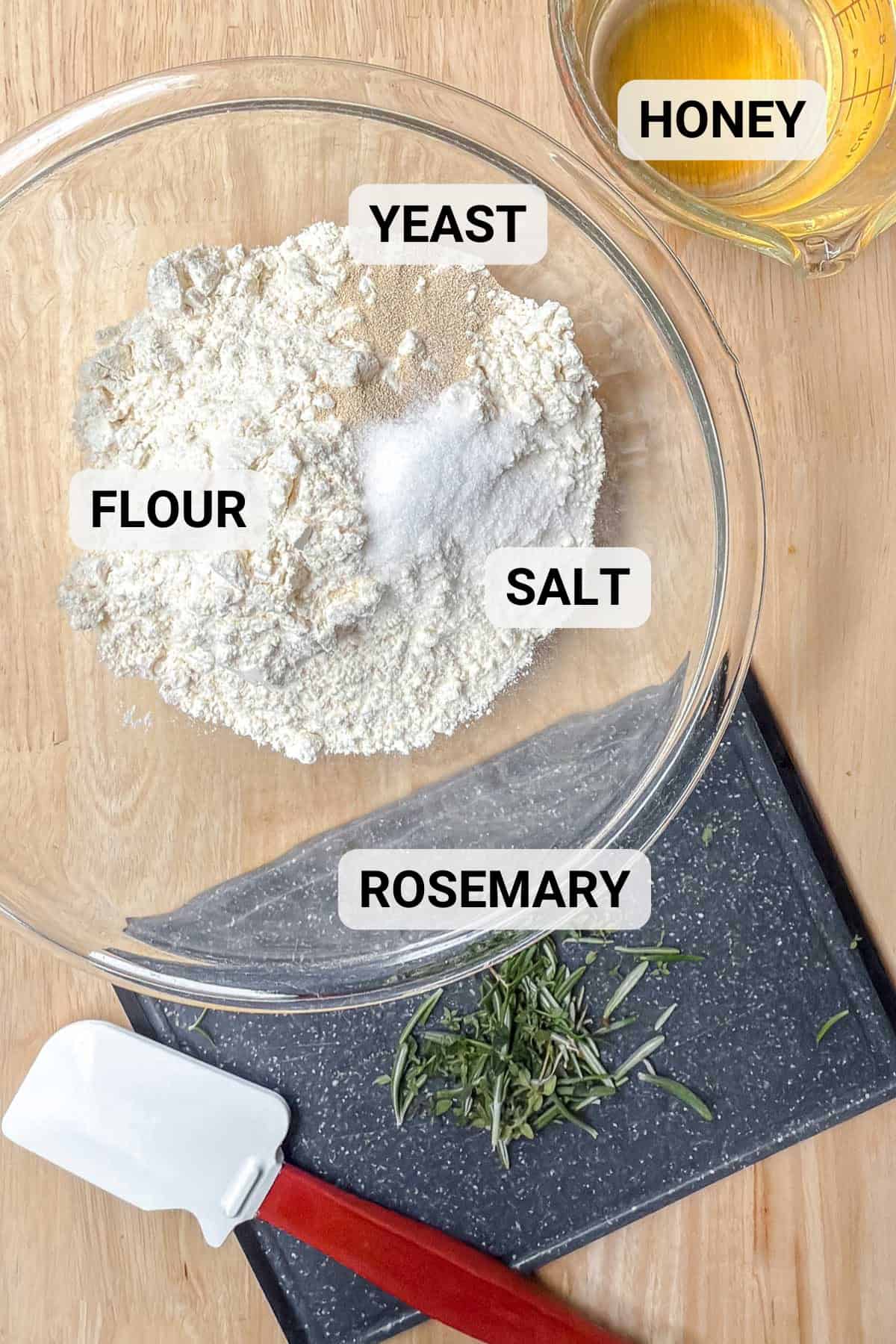 Ingredients for rosemary bread on a wooden surface with freshly chopped rosemary.